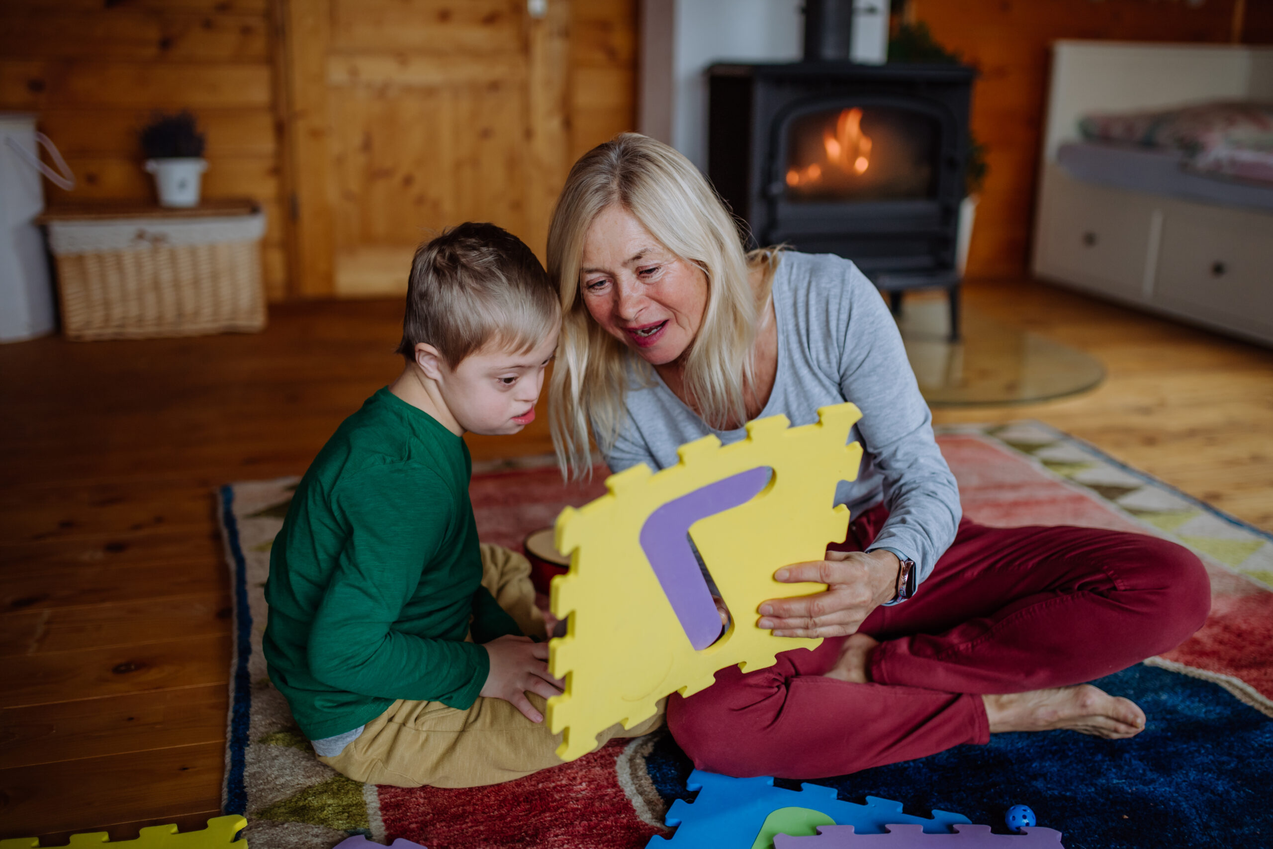 Boy with Down syndrome sitting on floor and playing with his grandmother at home A child and adult playing with puzzle pieces