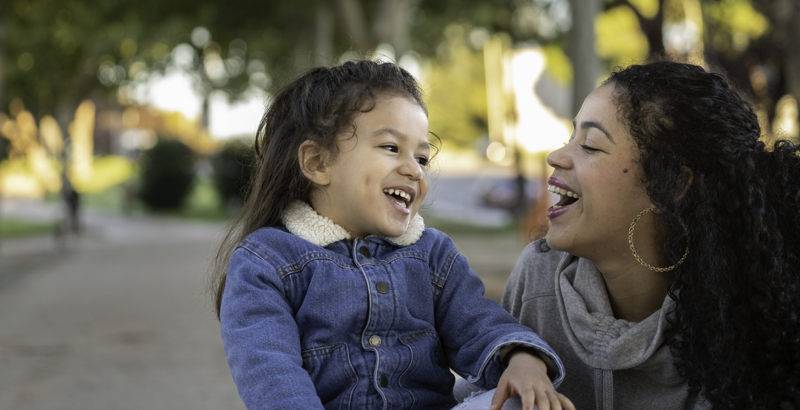 Portrait of latin mother and daughter sharing a moment of joy and laughter together in a park, enjoying quality time A child and adult laughing together outdoors