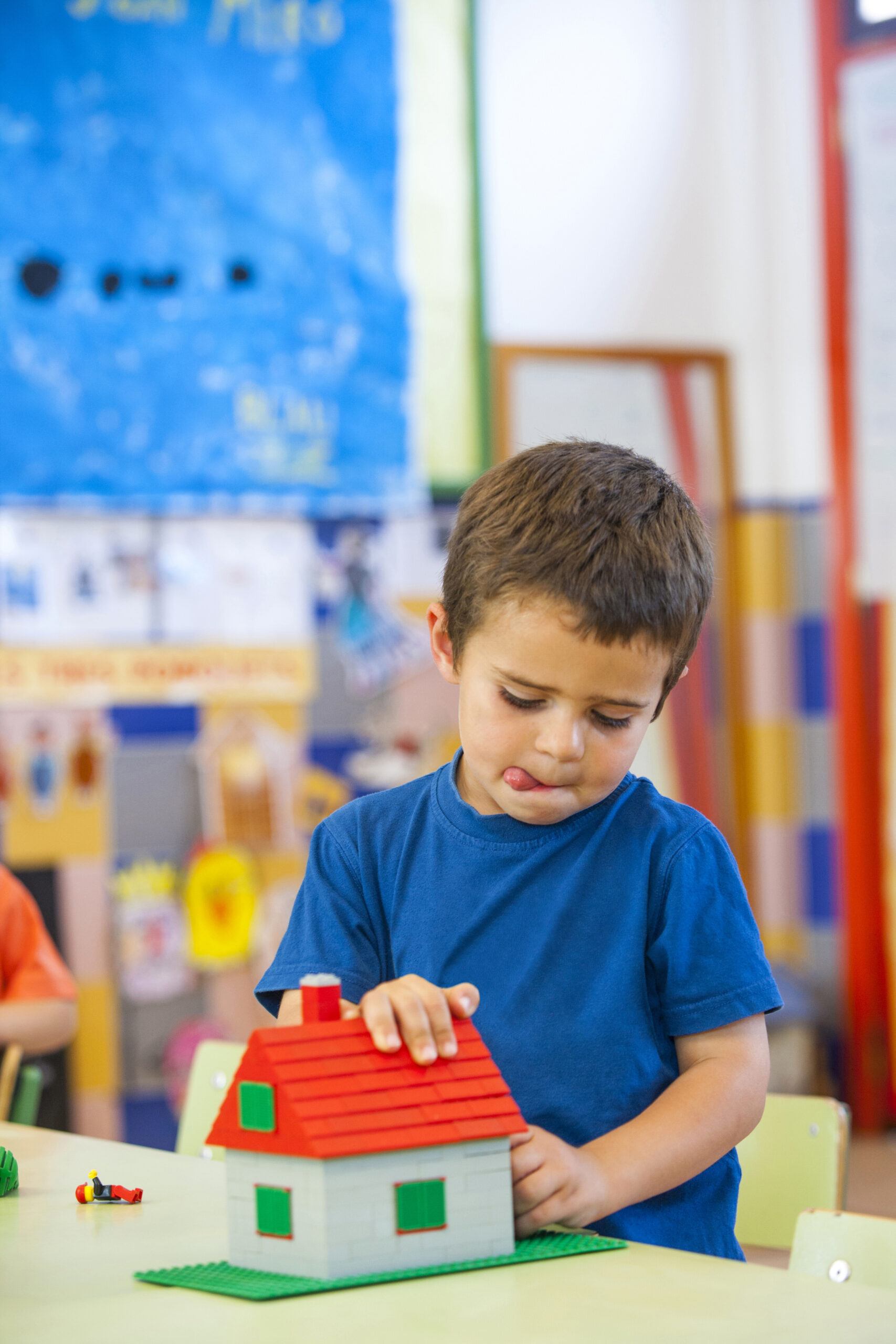 Preschool boy with tongue out building a toy block house in classroom A child building a toy house with blocks