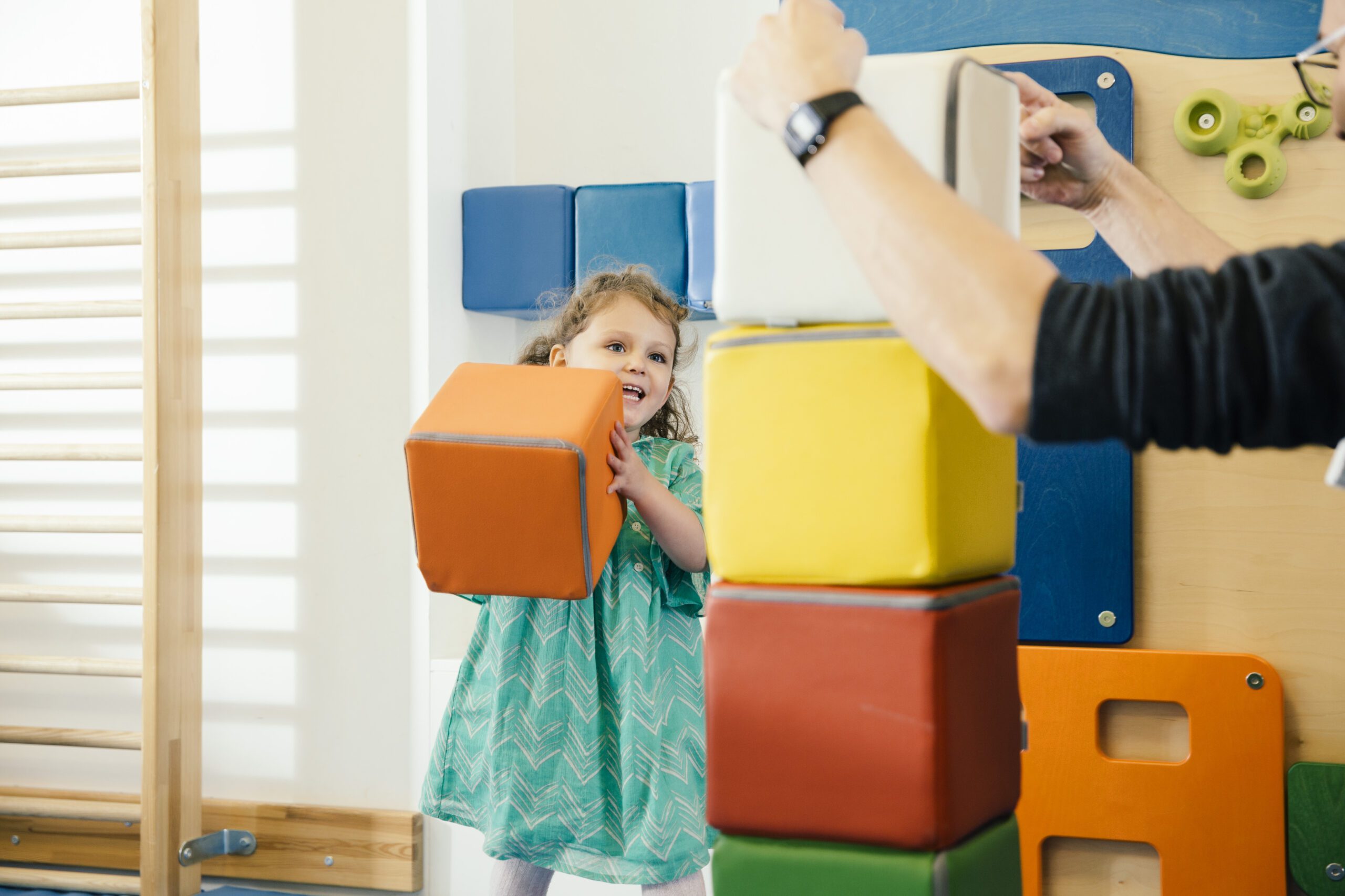 Happy little girl lifting up a soft building block in gym room of a kindergarten A child playing with a large soft building block